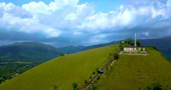 Timelapse - drone ascending over the lush green hill with a big cross into clouds. Mount Tapyas in Coron Town, Philippines.