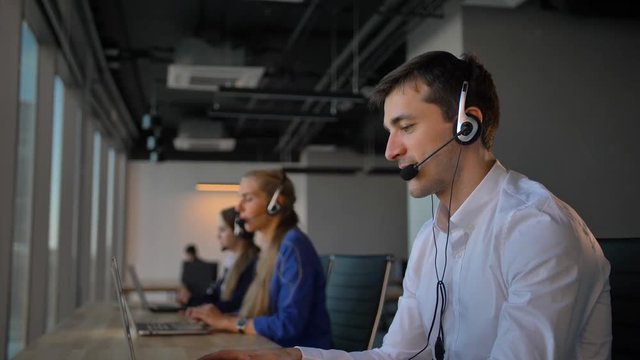 Attractive worker in office call center talking with client and then smile to camera. Concept of successful and cheerful solving of customer problems online.