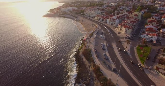 Drone shot folowing a white car on a costal road - Marginal in Parede, Lisbon, Portugal