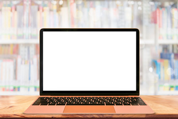 Mockup of laptop on wood table with blurred many books in library background.