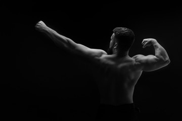 Fototapeta na wymiar Bodybuilder black and white portrait. Muscular man stands with his back. One hand shows up, the other hand with a big biceps. Man unrecognizable