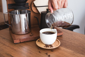 Closeup image of a hand pouring drip coffee into a white mug on vintage wooden table