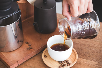 Closeup image of a hand pouring drip coffee into a white mug on vintage wooden table
