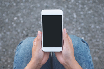 Top view mockup image of hand holding white mobile phone with blank black screen while sitting on the street