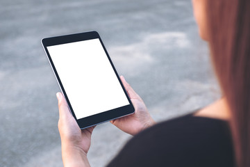 Mockup image of a woman holding and looking at black tablet pc with blank white screen with street background