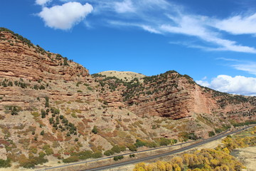 Beautiful hillside with rock faces and shrubs and trees.bright blue sky with a few clouds. a small country road and train tracks run in the foreground