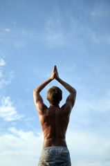 guy does yoga and stands in a meditative pose against a blue cloud sky