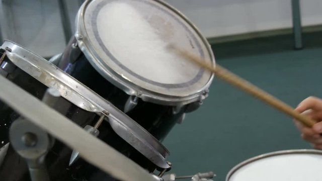The teenager is learning to play drum set. Drum sticks knock on different drums cymbals
