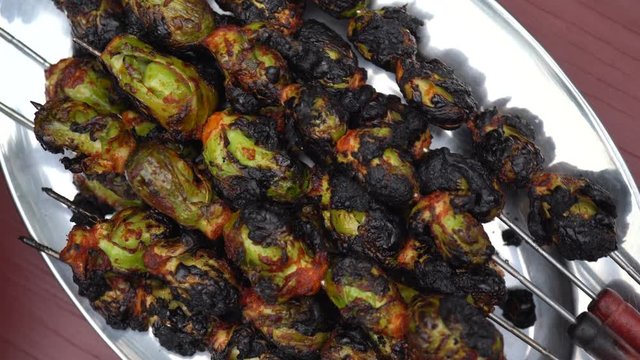 Turning closeup of brussels sprouts skewered on a silver platter.