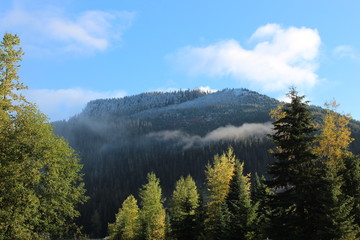 Snoqualmie Pass ,Washington, The first snow of the year its just a dusting . The clouds in the blue sky and the fog along the mountain side. the trees are showing fall colors .