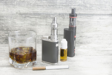 Whiskey in a glass with an e-cigarette and liquid for it on a gray stone background  