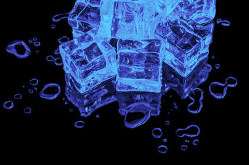 A hill of blue ice cubes on a black glass with water drops around.