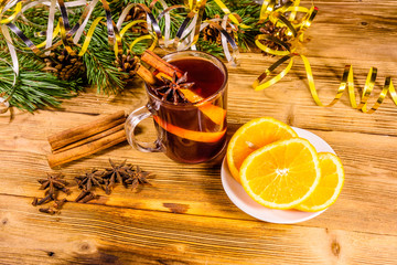 Cup of mulled wine with cinnamon, christmas decorations, sliced orange and fir tree branches on wooden table