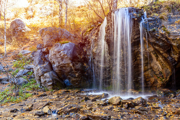 A  small waterfall in the mountains among the autumn forest. Golden autumn.