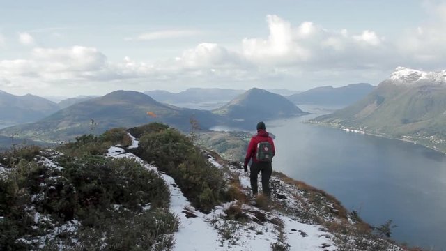 A shot of a woman walking on the top of a mountain in Norway, overlooking the fjords and a little town.