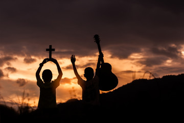 Two children holding christian cross and guitar with light sunset background,christian concept.