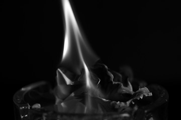 A piece of paper burning in a glass ashtray close up. Black and white