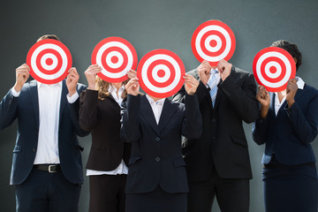 Group Of Businesspeople Hiding Their Faces Behind Dartboard
