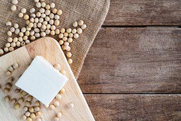 fresh white soft Japanese tofu on wooden plate with soy bean on gunny sack cloth, top view, copy...