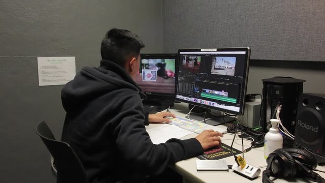 Young male asian boy editing video on computer. Blue jacket student uses technology in media lab. Time lapse.