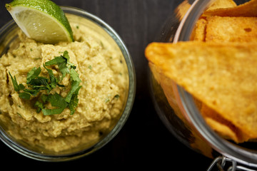 bowl of fresh delicious guacamole and a jar of nachos on an old black wooden table in a pub