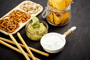 bowl of guacamole jar with nachos and salty snacks on an old black wooden table in a pub