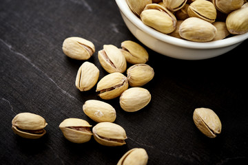 spilled delicious pistachios next to a white bowl on an old wooden black table in a pub