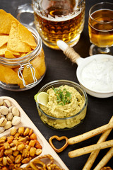 beer and a bowl of guacamole with nachos and salty snacks on an old black wooden table in a pub
