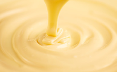 White chocolate. Pouring melted liquid white chocolate. Closeup of molten liquid hot chocolate swirl. Confectionery