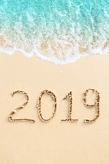New Year 2019 handwritten on the sandy beach with blue ocean wave