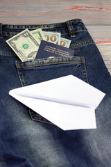Blue jeans back pocket look - dollars and passport. next to the pocket is a white paper plane.