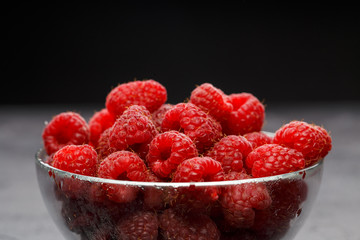 Photo of raspberries in transparent glass cup on black background