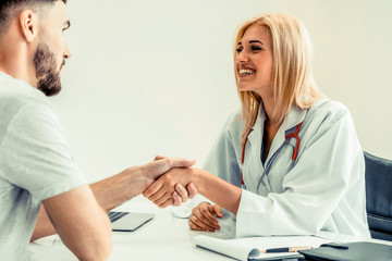 Woman doctor doing handshake with male patient in hospital office room. Healthcare and medical...