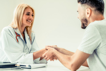 Woman doctor doing handshake with male patient in hospital office room. Healthcare and medical...