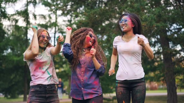 Slow motion of cheerful girls multi-ethnic group dancing then throwing paint powder at outdoor party in park. Youth culture, happy people and fun concept.