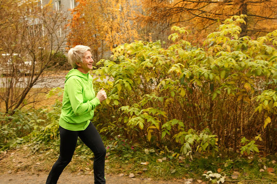 Senior Woman Doing Sport Outdoors,exercising On A Forest Road In The Autumn .Pensioner Woman Sport