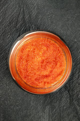 A top shot of red caviar in a jar on a black background with copyspace
