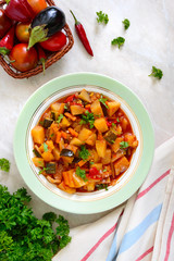 Delicious vegetable stew in a bowl on the table. Stewed potatoes, eggplants, zucchini, onions, carrots in spicy tomato sauce with greens.
