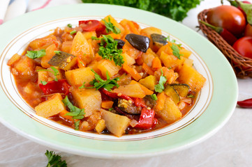 Delicious vegetable stew in a bowl on the table. Stewed potatoes, eggplants, zucchini, onions, carrots in spicy tomato sauce with greens.