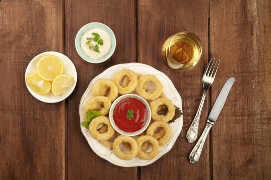 A top shot of squid rings with two sauces, lemon wedges, white wine, and a place for text