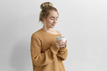 Isolated image of gorgeous charming young female with hair knot holding large mug enjoying freshly...