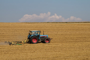 Obraz premium Traktor auf einem gemähten Feld im Sonnenschein