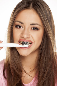 young woman brushing her teeth with electric tooth brush with black active charcoal toothpaste on white background