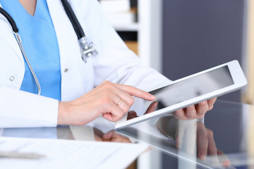 Woman doctor using tablet computer while standing straight in hospital office, closeup. Healthcare, insurance and medicine concept