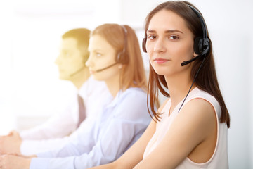 Naklejka premium Call center operators. Focus on young cheerful smiling woman in headset. Business and customer service concepts