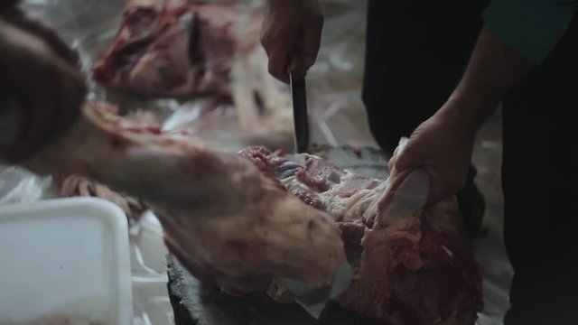 Two men chopping up raw meat. One holds the piece. The other one cuts it with a knife. A close-up