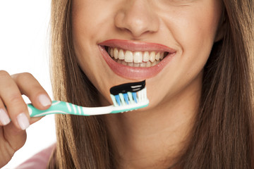 young woman holding tooth brush with black active charcoal toothpaste on white background