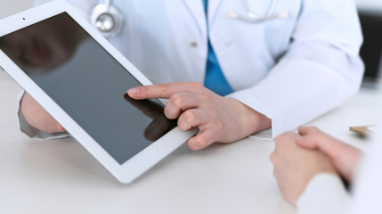  Closeup of a doctor and  patient  sitting at the desk. Physician pointing into tablet pc. Medicine...