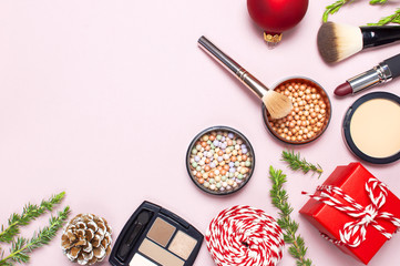 Various cosmetic products for make-up, blusher, powder, brushes, lipstick, eyeshadow and Christmas gift, fir branches, red ball on pink background Flat lay top view New year concept, winter decoration