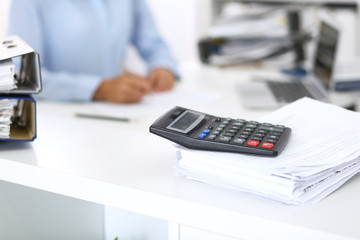 Fototapeta premium Calculator and binders with papers are waiting to be processed by business woman or bookkeeper back in blur. Internal Audit and tax concept